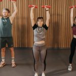 Three adults exercising with dumbbells in a gym setting, promoting fitness and healthy lifestyle.